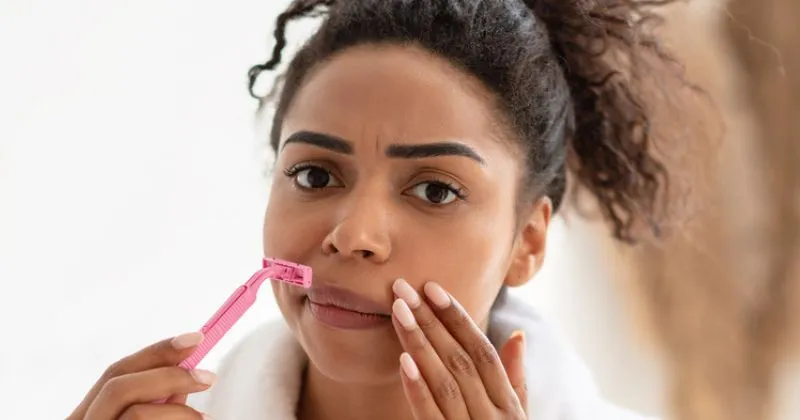 A young woman using a razor for facial hair